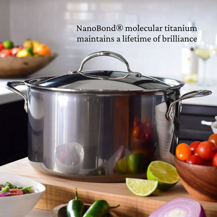 A NanoBond 10-Piece Titanium Precision Saucepan from the cookware set sits on a kitchen counter. Fresh tomatoes and limes are nearby, and text above reads, NanoBond Technology ensures a lifetime of brilliance.