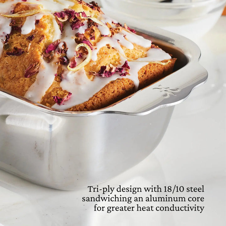 A cake with white icing and dried rose petals sits elegantly in an OvenBond Tri-Ply 3-Piece Baking Set pan by Hestan Provisions, featuring a tri-ply design with 18/10 steel sandwiching an aluminum core for superior heat conductivity and warp resistance.