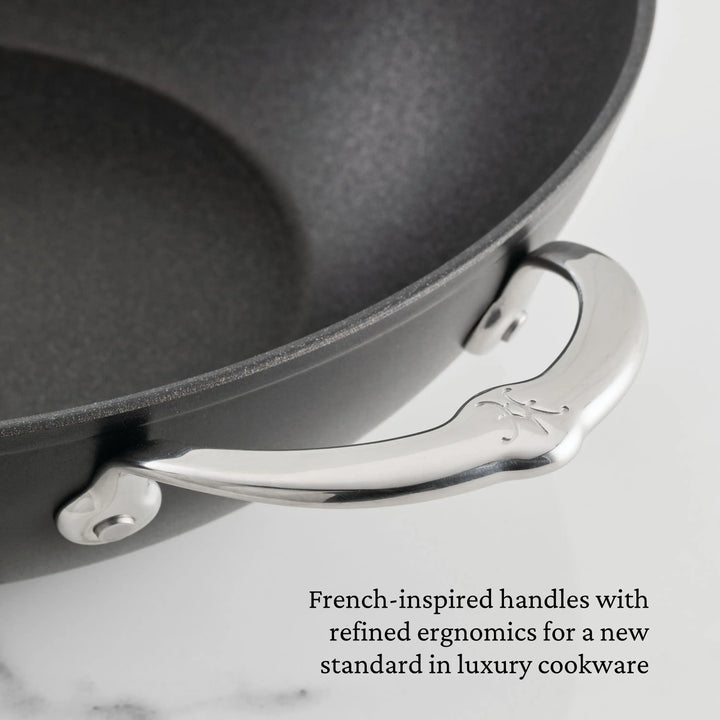 Close-up of a TITUM® Fusion TITUM Nonstick Cookware Set pan featuring a curved stainless steel handle with two rivets. Text notes French-inspired, ergonomic handles handcrafted in Italy for this luxury 10-piece nonstick set.