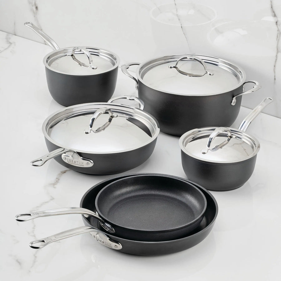 The TITUM® Fusion TITUM Nonstick Cookware Set, 10-Piece, features black pans and pots with stainless steel handles and lids, including two nonstick pans, three lidded saucepans, and a large lidded pot, shown on white marble.