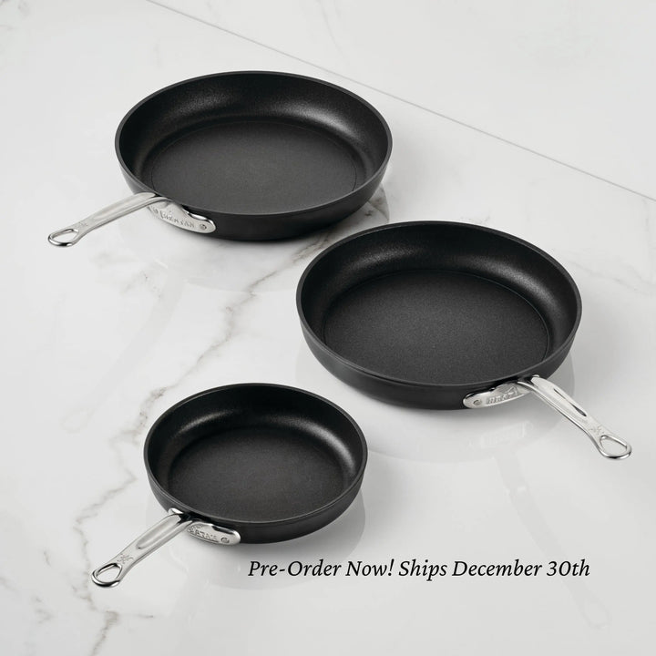 Three black TITUM® Fusion Nonstick Open Skillets in different sizes with silver handles are displayed on a white marble surface. Induction compatible, handcrafted in Italy. Pre-order now! Ships December 30th.