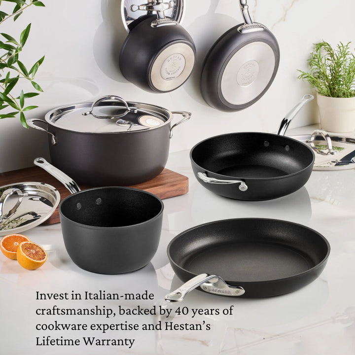 TITUM® Fusion TITUM Nonstick Saucepans with Lids, featuring matte black finish, are showcased on a white countertop with citrus and herbs. Italian craftsmanship is highlighted in this elegant cookware display.