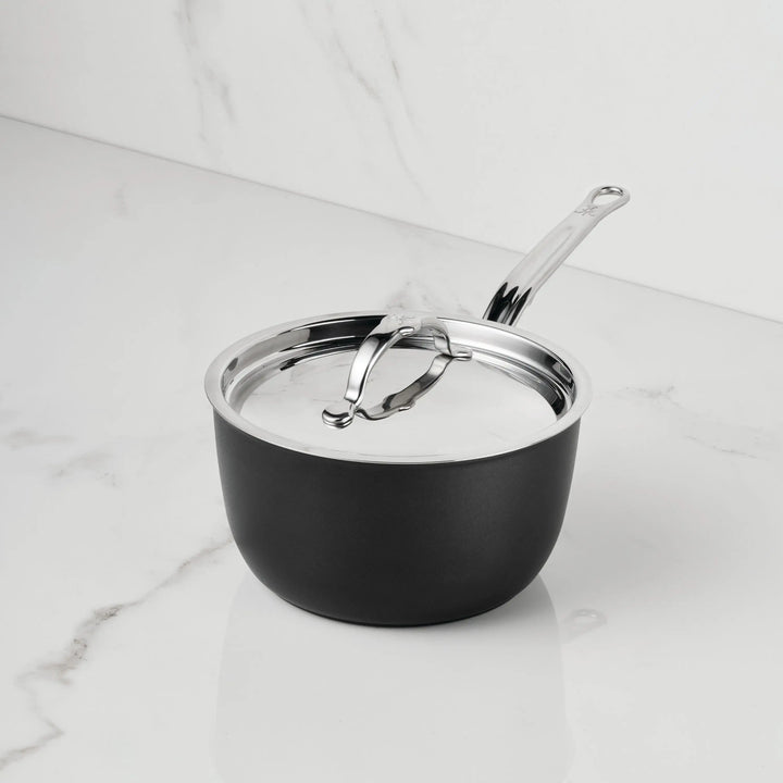 The TITUM® Fusion TITUM Nonstick Saucepan with stainless steel handle and lid, handcrafted in Italy, rests on a white marble countertop with gray veining.