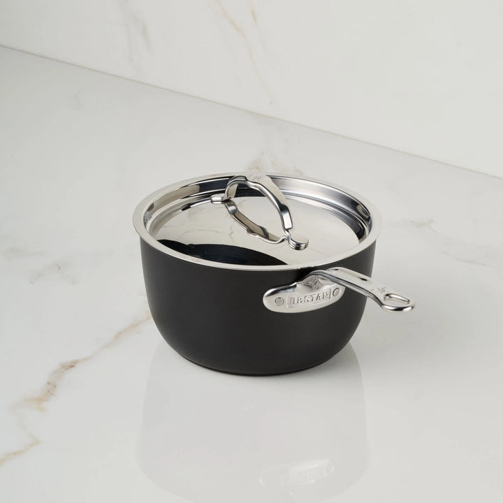 A small black TITUM® Fusion TITUM Nonstick Saucepan with a metal handle engraved “BREVILLE” and matching lid sits on a white marble countertop. Induction compatible, it’s perfect for versatile, modern kitchens.
