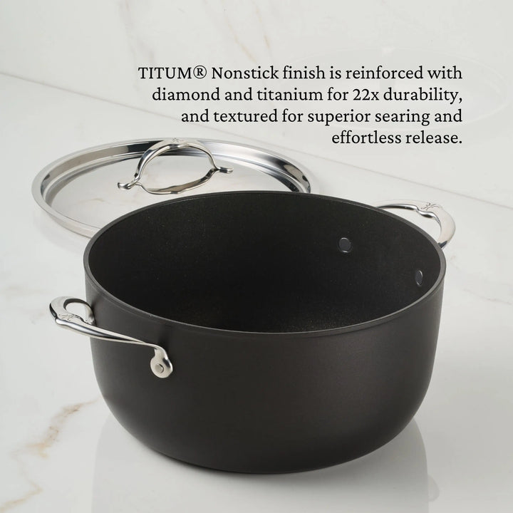 A black TITUM® Fusion TITUM Nonstick Stock Pot with Lid, 8-Quart, featuring two metal handles, sits on a white countertop beside its stainless steel lid. Text above highlights its reinforced nonstick finish and exceptional durability.