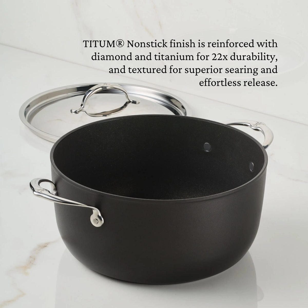 A black TITUM® Fusion TITUM Nonstick Stock Pot with Lid, 8-Quart, featuring two metal handles, sits on a white countertop beside its stainless steel lid. Text above highlights its reinforced nonstick finish and exceptional durability.