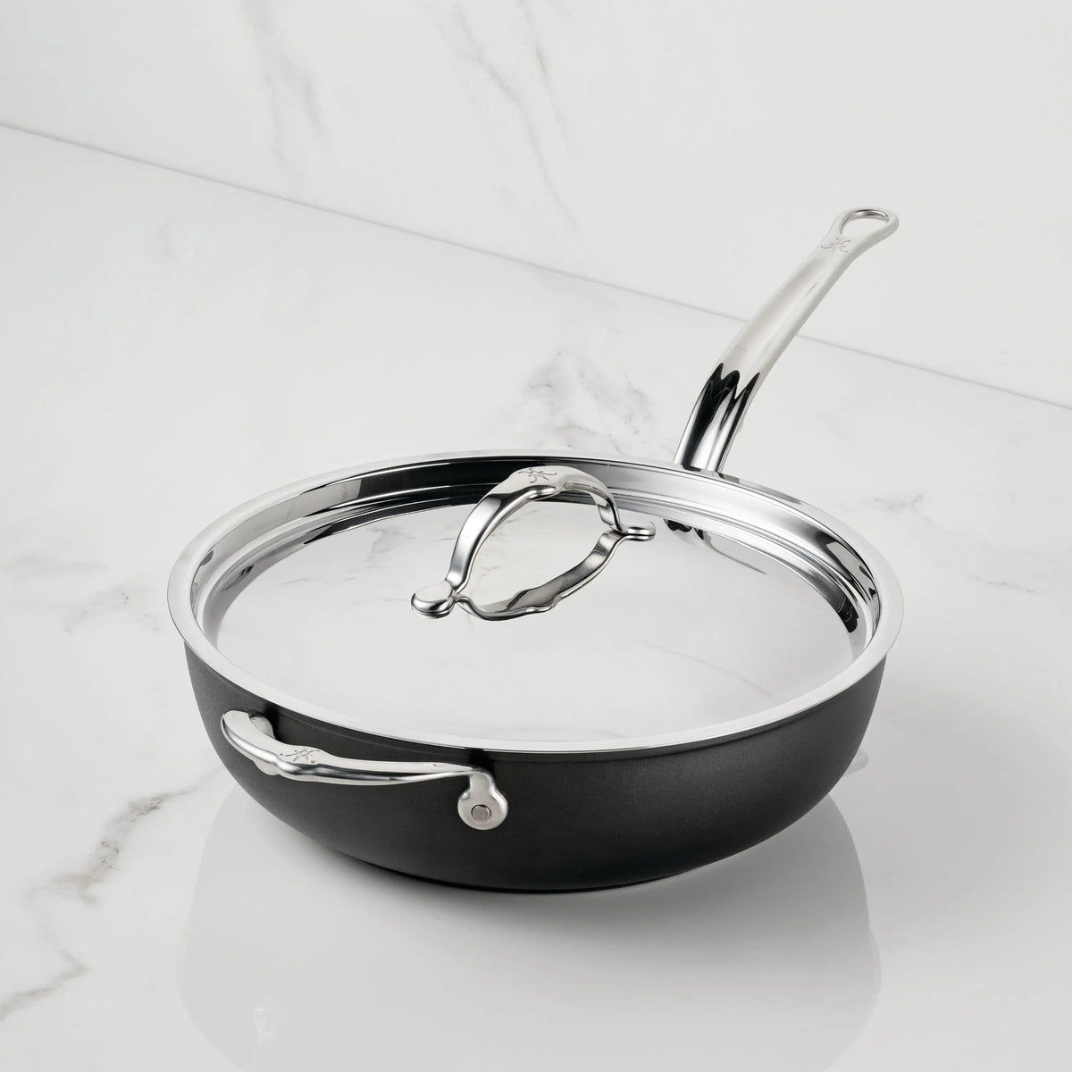 The TITUM® Fusion TITUM Nonstick Essential Pan with Lid, 4.5-Quart, featuring a black nonstick finish and stainless steel handle, handcrafted in Italy, sits elegantly on a white marble countertop.