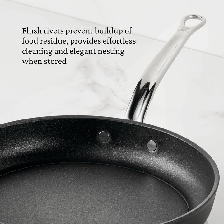 The TITUM® Fusion TITUM Nonstick Open Skillets, handcrafted in Italy with a metal handle, rest on marble. Flush rivets on the inner surface make cleaning and storage easier, as highlighted in the text.