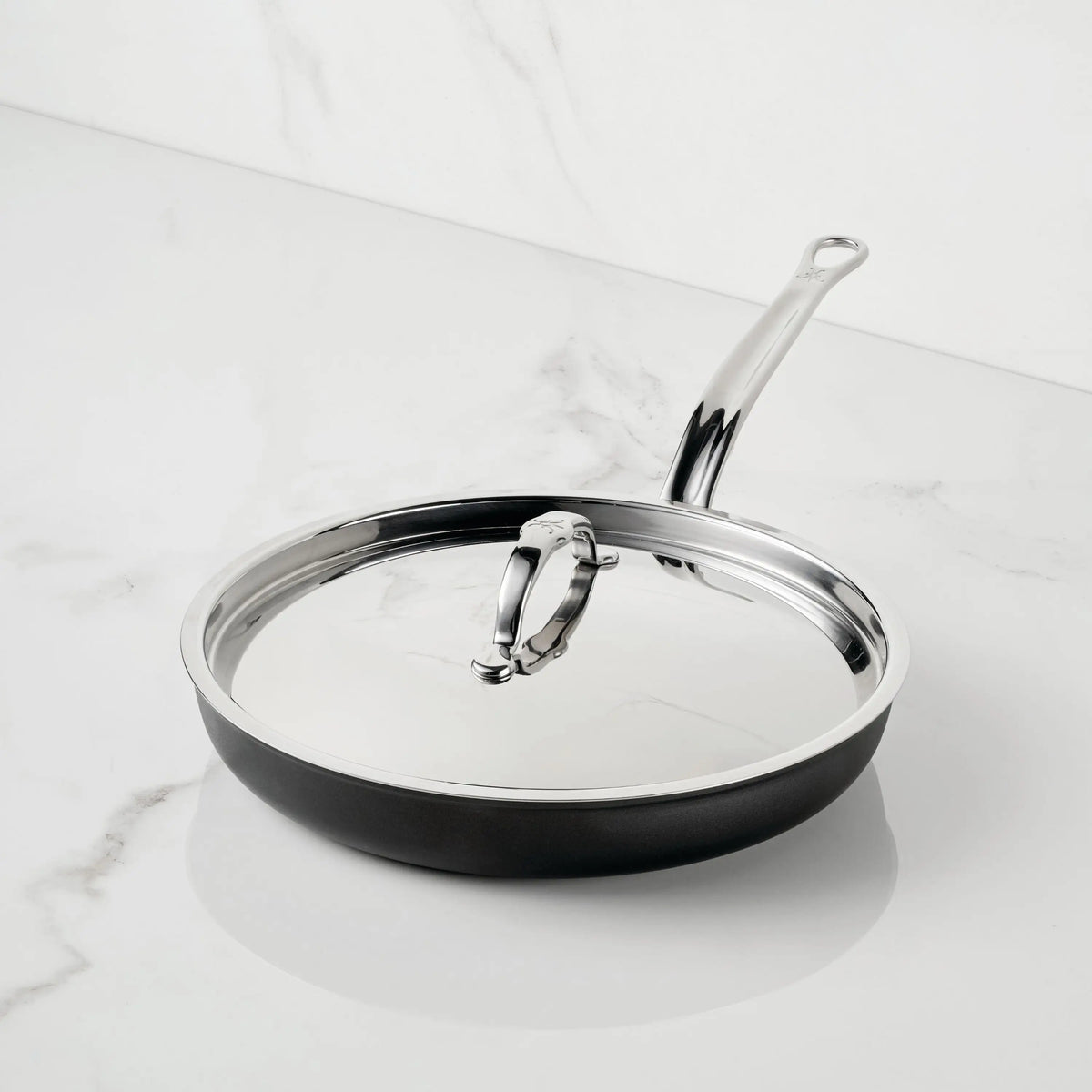 The TITUM® Fusion TITUM Nonstick Skillet with Lid, 11-inch, featuring a long handle, rests on a white marble countertop—highlighting its handcrafted in Italy quality and durable stainless steel design.