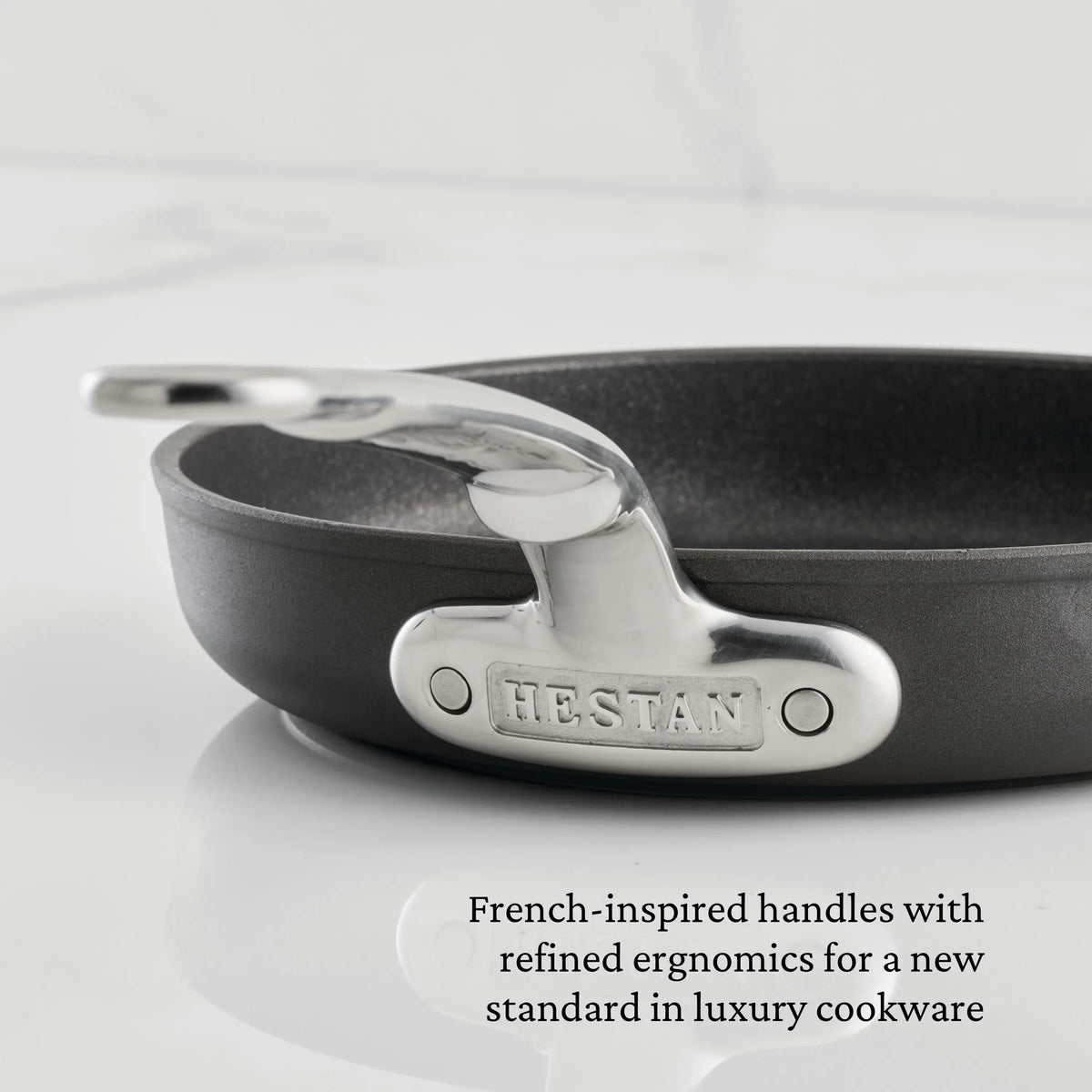Close-up of the TITUM® Fusion Nonstick Skillet with Lid, 11-Inch. The shiny, French-inspired metal handle offers refined ergonomics, elevating this handcrafted-in-Italy pan to a new standard in luxury cookware.