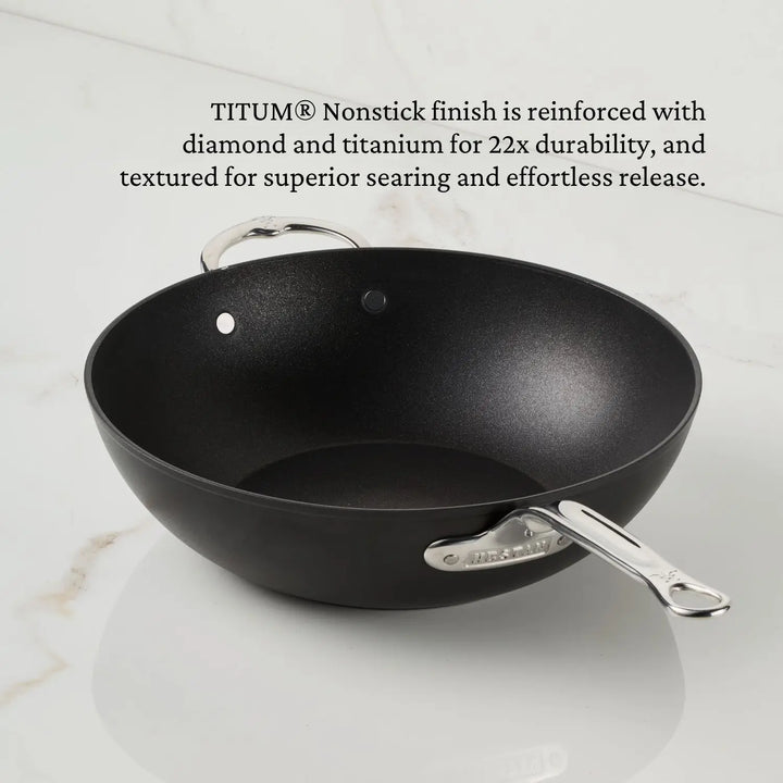 A 12.5-inch TITUM® Fusion TITUM Nonstick Wok with stick handle and dome lid rests on a white countertop, showcasing its durable, textured TITUM® Nonstick finish and Italian craftsmanship.