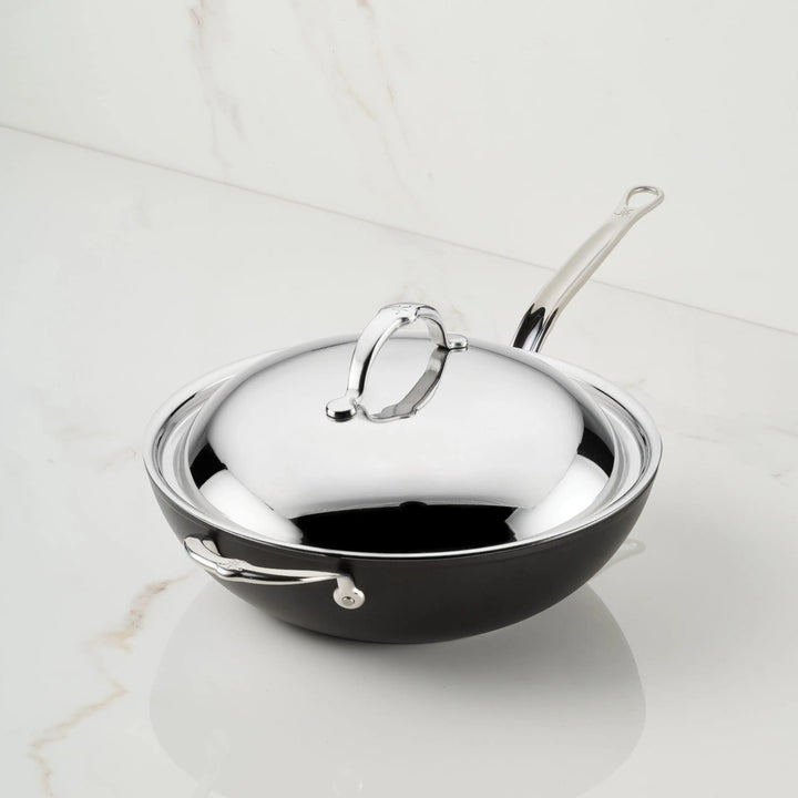 A TITUM® Fusion 12.5-Inch Nonstick Wok with stick handle and dome lid sits on white marble, highlighting its durable Italian craftsmanship and stylish stainless steel design.