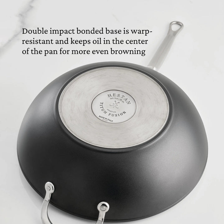 A TITUM® Fusion 12.5-Inch Nonstick Wok with Stick Handle and Dome Lid is shown upside down on a white surface, highlighting its durable brushed stainless steel base and Italian craftsmanship for even browning and warp resistance.