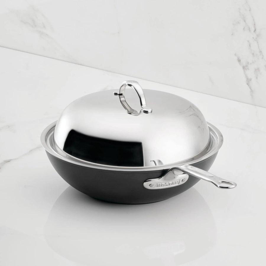 A TITUM® Fusion 12.5-Inch TITUM Nonstick Wok with stick handle and matching dome lid, featuring a large loop top handle, sits on a white marble countertop.