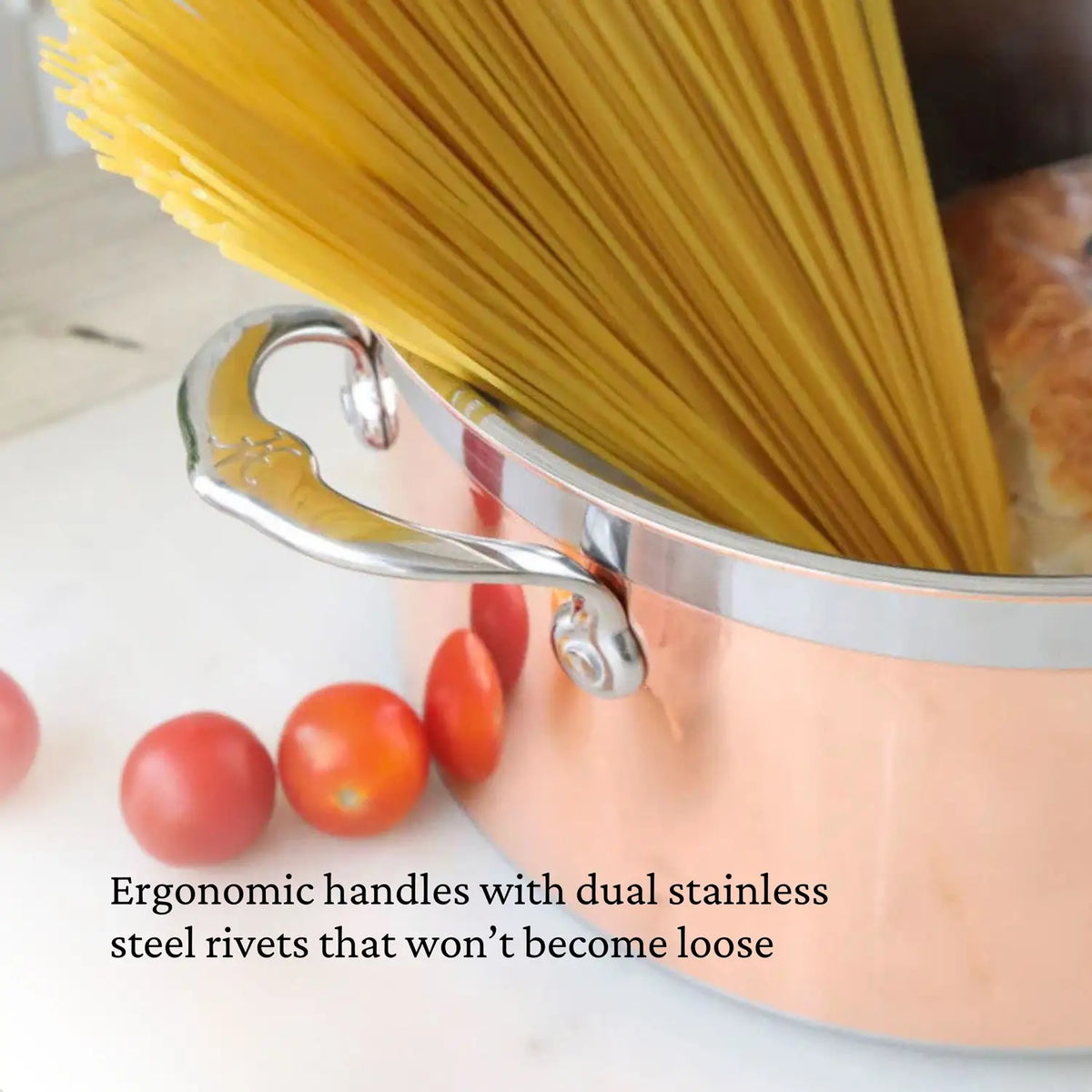 A CopperBond Copper Induction Soup Pot, 3-Quart with ergonomic stainless steel handles is filled with uncooked spaghetti, while red tomatoes are scattered nearby on a light surface. Text highlights its dual stainless steel rivets and induction compatibility.