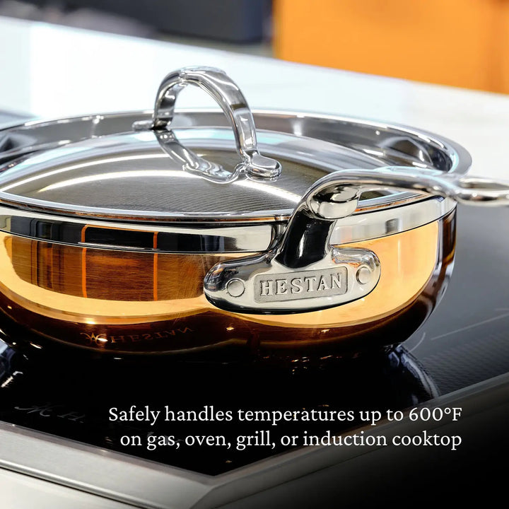 A Copper Induction Essential Pan by CopperBond, handcrafted in Italy, sits on the stove. The copper saucepan with a stainless steel lid features CopperBond on its handle and handles temperatures up to 600°F on gas, oven, grill, or induction cooktops.