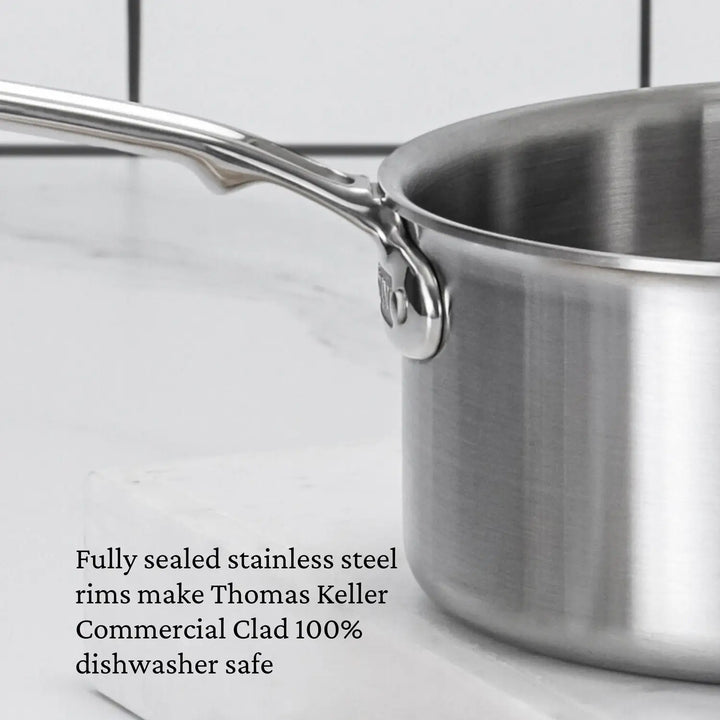 Close-up of a stainless steel saucepan with a long handle on white marble. Featuring ProCore Aluminum for professional performance and a polished finish. Text: Thomas Keller Insignia Commercial Clad Saucepans with fully sealed rims are 100% dishwasher safe.