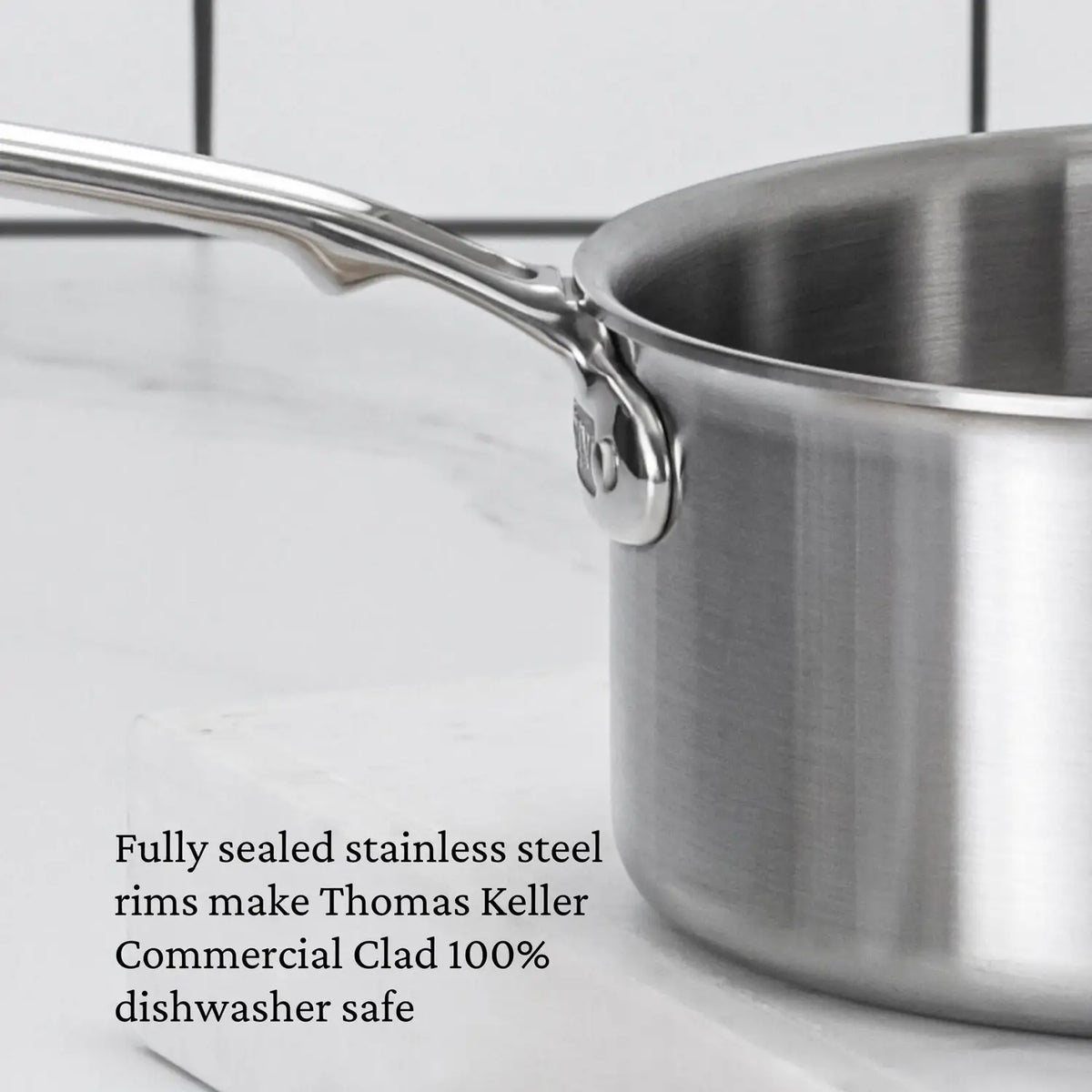 A close-up of the Thomas Keller Commercial Clad Stainless Steel Saucepan with handle on a white surface. Text highlights its fully sealed rims and 100% dishwasher safe design—ideal for professional results.