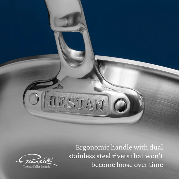 An upclose shot of the rear flange of the Thomas Keller Commercial Clad skillet displays the Hestan logo. The image shows the high-quality stainless steel rivets, highlighting the durability and Italian made craftsmanship. Text on image reads: "Ergonomic handle with dual stainless steel rivets that won’t become loose over time". 