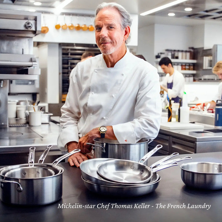 In a bustling professional kitchen, a chef in white attire is amidst Thomas Keller Insignias Commercial Clad Stainless Steel Skillets, famous for their outstanding heat conductivity. Text reads: Michelin-star Chef Thomas Keller - The French Laundry.