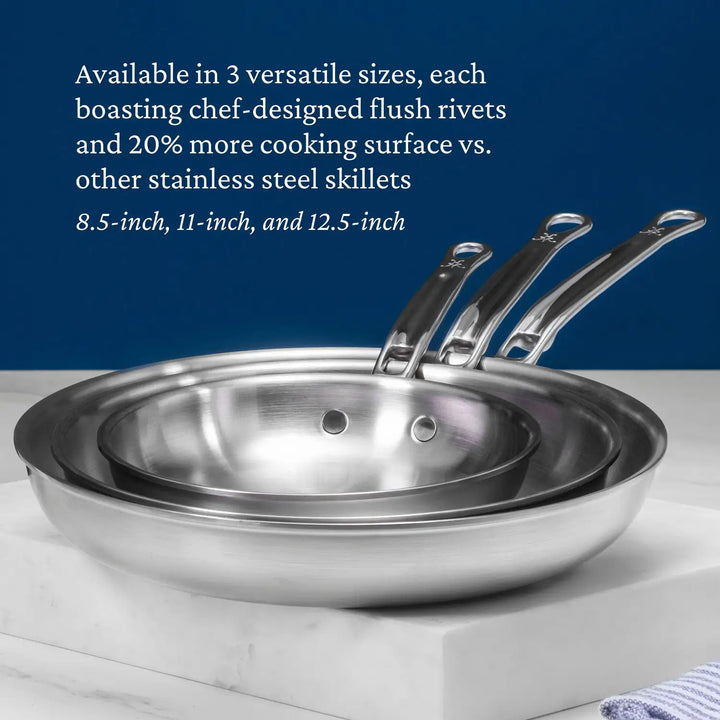 Three Thomas Keller Insignia Commercial Clad Stainless Steel Skillets with handles are stacked on a counter. Text highlights their heat conductivity and flush rivets, noting they provide 20% more cooking surface than other tri-ply skillets, available in 8.5-inch, 11-inch, and 12.5-inch sizes.