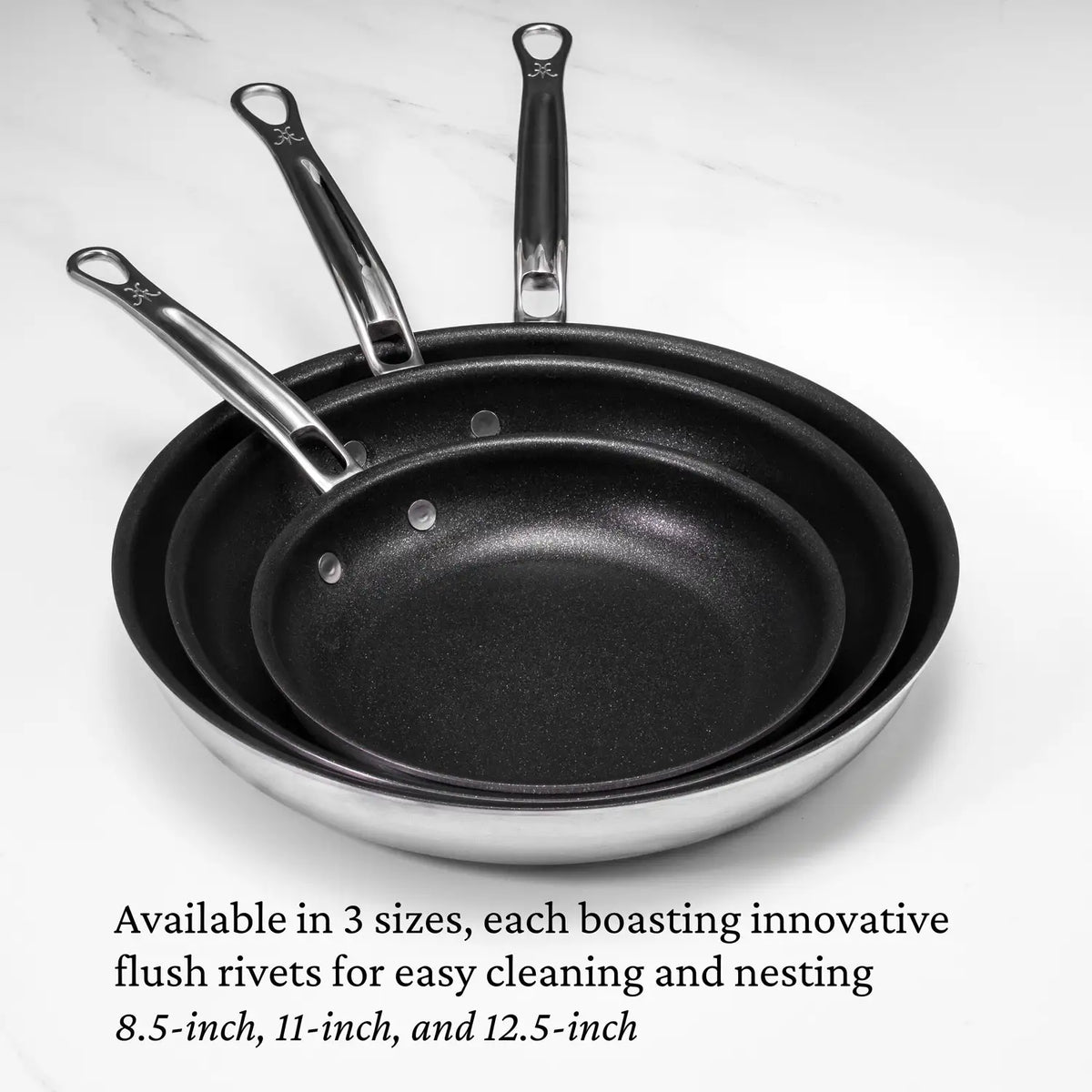 The Thomas Keller Commercial Clad Stainless Steel TITUM® Nonstick Skillets nest in 8.5-, 11-, and 12.5-inch sizes, each with metal handles and flush rivets for easy cleaning—ideal for professional culinary results.