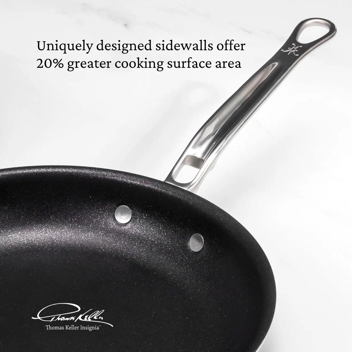 Close-up of a Thomas Keller Commercial Clad Stainless Steel TITUM® Nonstick Skillet with a shiny metal handle on a white surface. Above, it reads, “Uniquely designed sidewalls offer 20% greater cooking surface area.” Signature in lower-left corner.