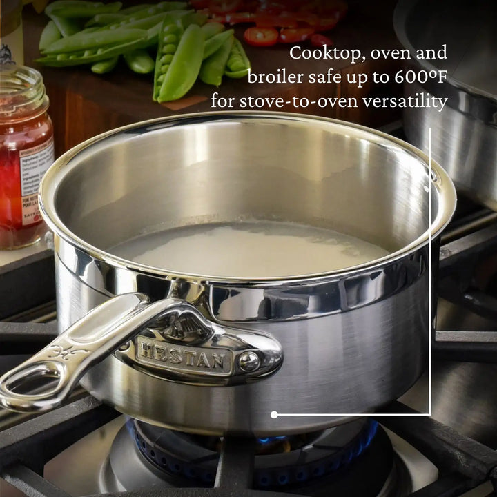 A ProBond Professional Clad Stainless Steel Saucepan filled with liquid is on a stovetop, showcasing its tri-ply aluminum core. Text overlay says, Safe for cooktop, oven, and broiler use up to 600°F. Shiny and reflective, green vegetables are seen in the background.