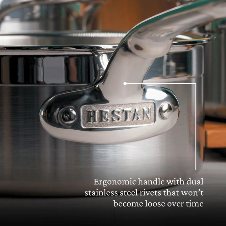 Close-up of a ProBond Professional Clad saucepan handle, crafted for comfort with an ergonomic design. The stainless steel handle is secured by dual rivets for durability and features a tri-ply aluminum core for optimal heat distribution, engraved with HESTAN.