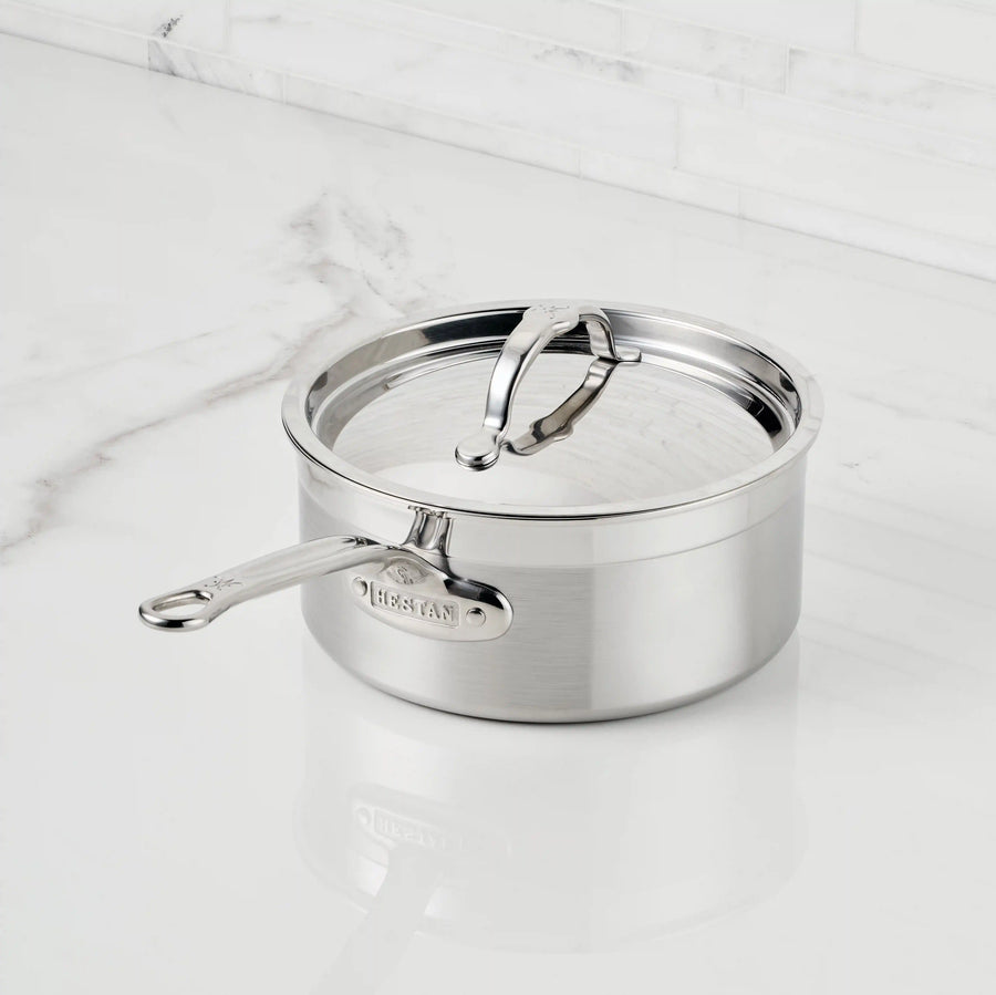 A ProBond® Forged™ Professional Clad Stainless Steel Saucepan, featuring a tri-ply body and polished handle with lid, rests on a white marble countertop. The “ProBond® Forged™” brand is engraved on the handle.