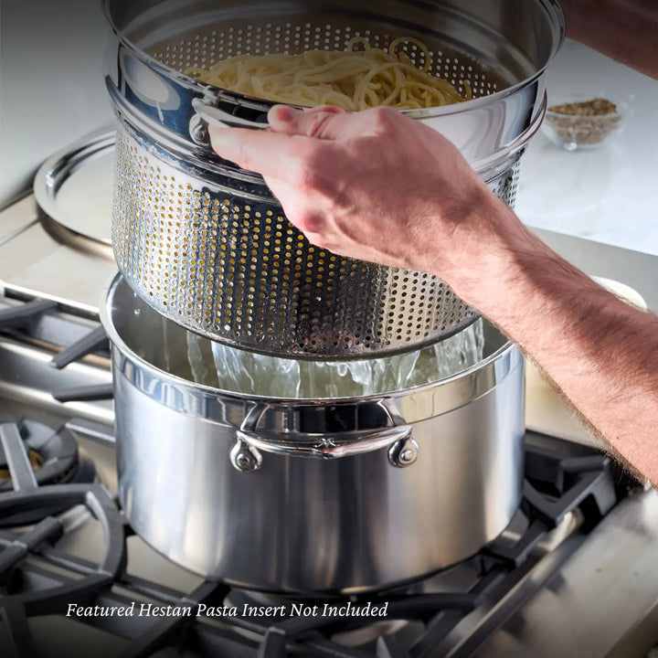 A person lifts a perforated pasta insert with spaghetti from an 8-quart stainless steel stockpot on the stovetop. This ProBond cookware, with two handles, shines in the sleek Hestan tri-ply collection. Caption: Featured Hestan Pasta Insert Not Included.