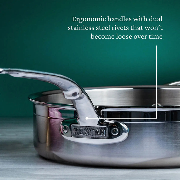 Close-up of the ProBond Professional Clad Stainless Steel Covered Sauté Pan, featuring a secure tri-ply body handle attached with dual stainless steel rivets, resting against a green background on a light gray surface to highlight its sleek design.