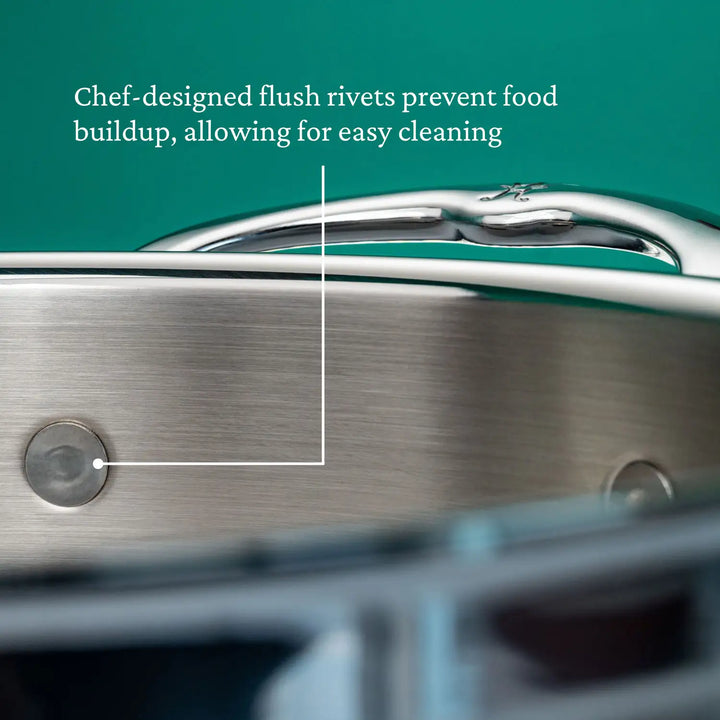 Close-up of the ProBond Professional Clad Stainless Steel Braiser with Lid (3.5-Quart) featuring flush rivets to prevent food buildup for easy cleaning. The handle stands out against a green background, highlighting its style and functionality.