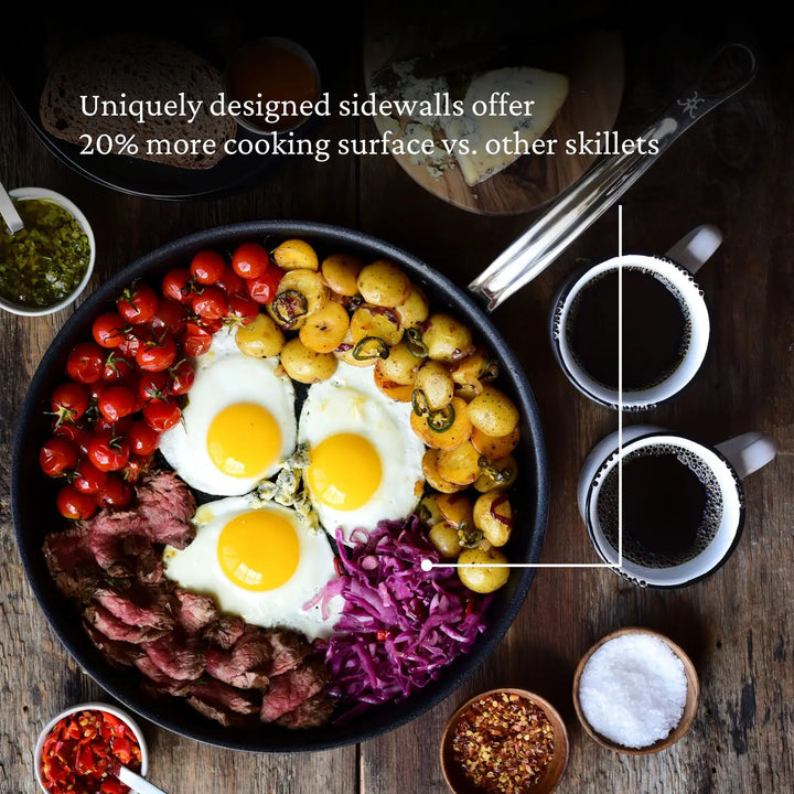 A ProBond Professional Clad Stainless Steel TITUM® Nonstick Skillet, filled with steak, eggs, cherry tomatoes, potatoes, and red cabbage, allows for a seamless culinary experience with its unique sidewalls offering 20% more cooking surface. It’s paired with two cups of black coffee alongside salt and spices.