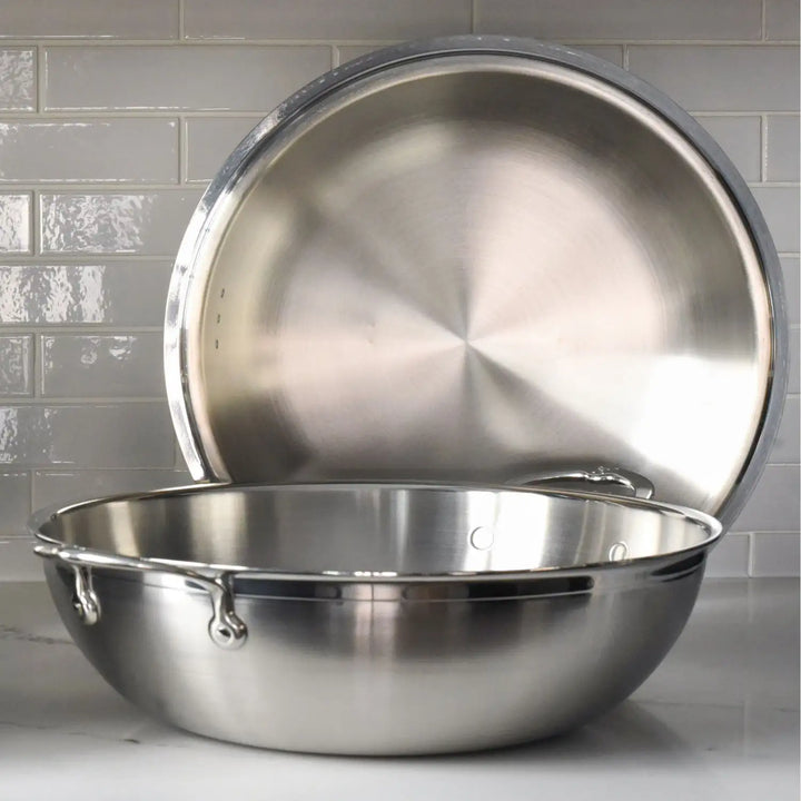 A ProBond 14-inch Professional Clad Stainless Steel Wok with a tri-ply body and lid is set against light gray subway tiles. The wok features sturdy handles on each side.