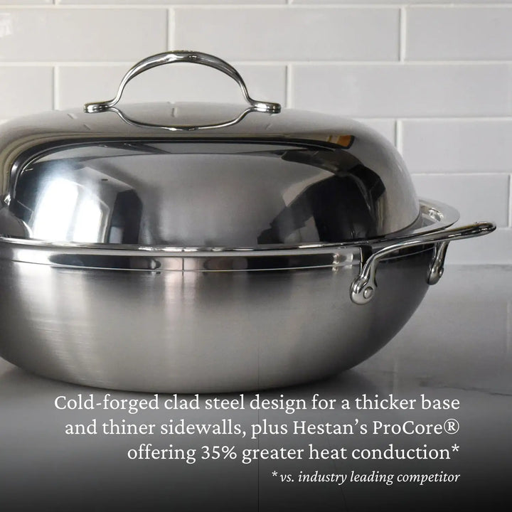 A 14-inch ProBond Professional Clad Stainless Steel Wok is on a kitchen counter, surrounded by white subway tiles. Its tri-ply body boasts Hestan’s ProCore® innovation for 35% greater heat conduction, highlighting its efficient cold-forged clad steel design.