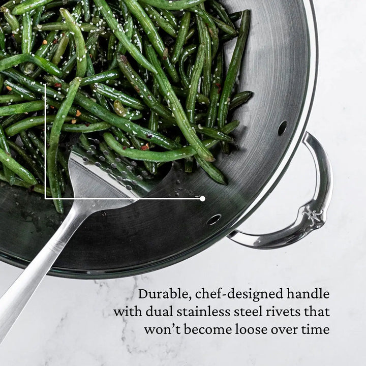 The 14-inch ProBond Professional Clad Stainless Steel Wok is filled with cooked green beans and garlic, topped with sesame seeds and chili flakes. Inside, a spatula rests. The text emphasizes the durable, chef-designed handle with dual stainless steel rivets and a robust tri-ply body.