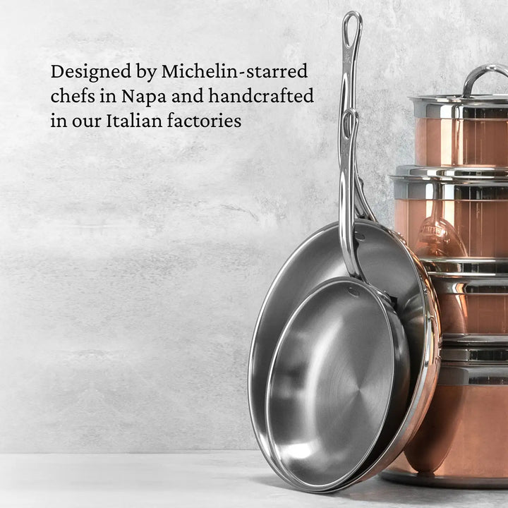 Two CopperBond Copper Induction Skillets with long handles rest against a stack of copper cookware. A light gray textured wall in the background reads, Designed by Michelin-starred chefs in Napa and handcrafted with induction-compatible, 5-layer construction in our Italian factories.