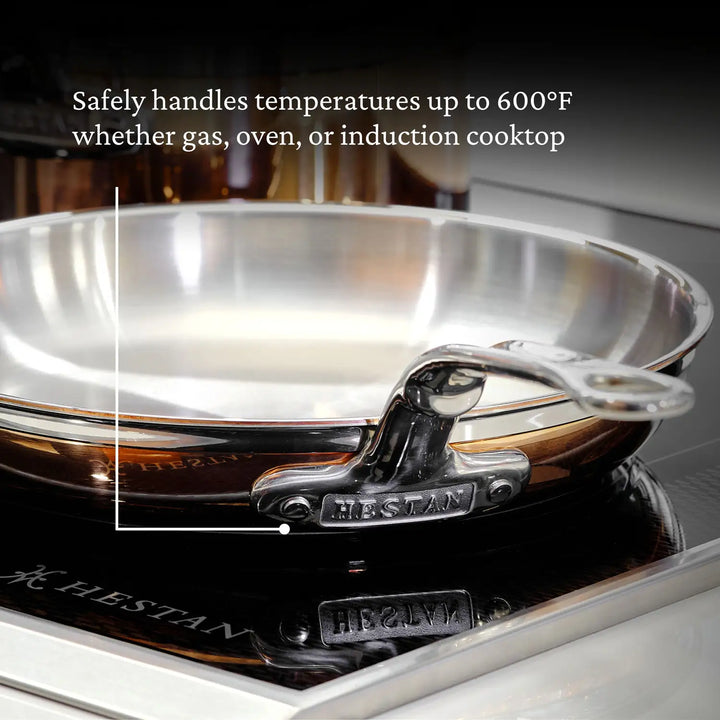 The CopperBond Copper Induction Skillet, with its copper core, elegantly rests on the stovetop. Its handle bears the distinctive branding. This versatile, induction-compatible cookware withstands temperatures up to 600°F on gas, oven, or induction cooktops.