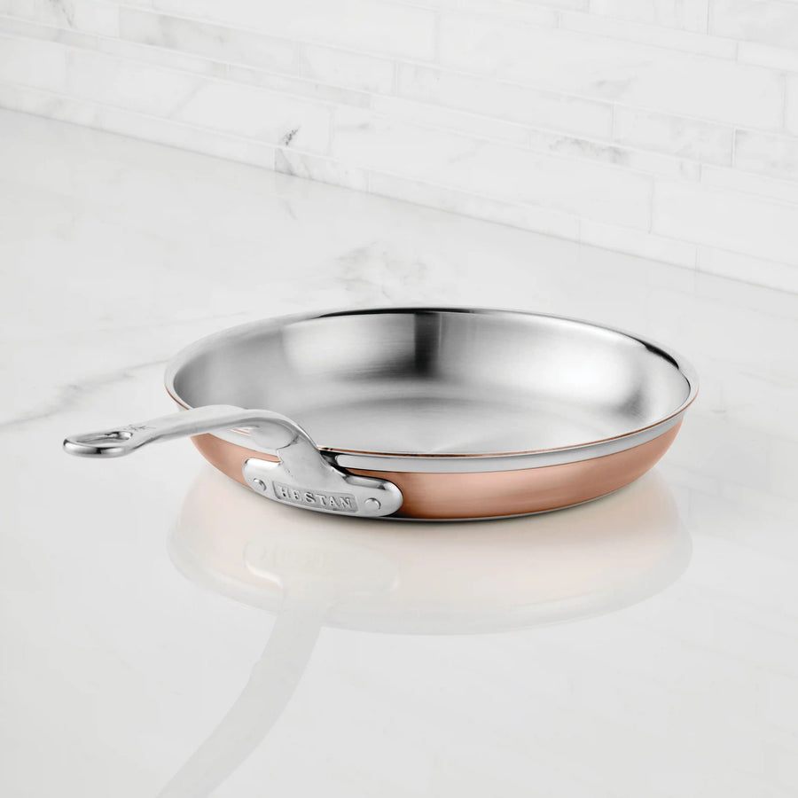 A CopperBond Copper Induction Skillet with 5-layer construction and a metal handle rests on a white marble countertop, backed by a white tile backsplash.