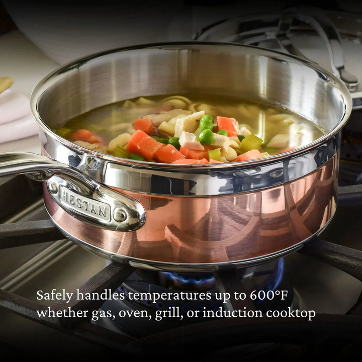 The CopperBond Copper Induction Saucepan features a 100% copper core and stainless steel handle, containing soup with noodles, carrots, and peas. It safely withstands temperatures up to 600°F on gas, ovens, grills, or induction cooktops.