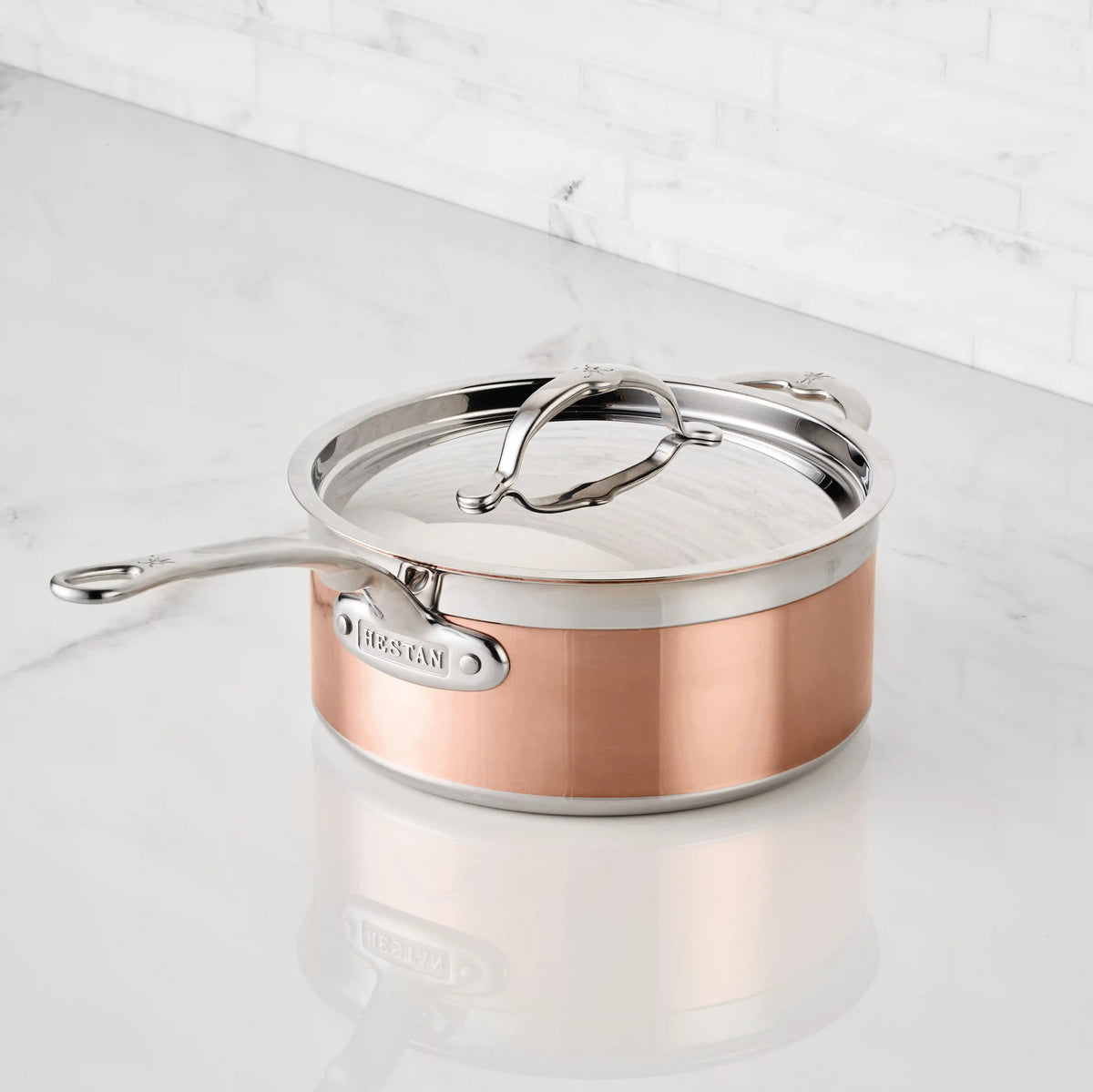 A CopperBond Copper Induction Saucepan sits on a glossy white marble countertop, with a white marble tiled wall as the background.