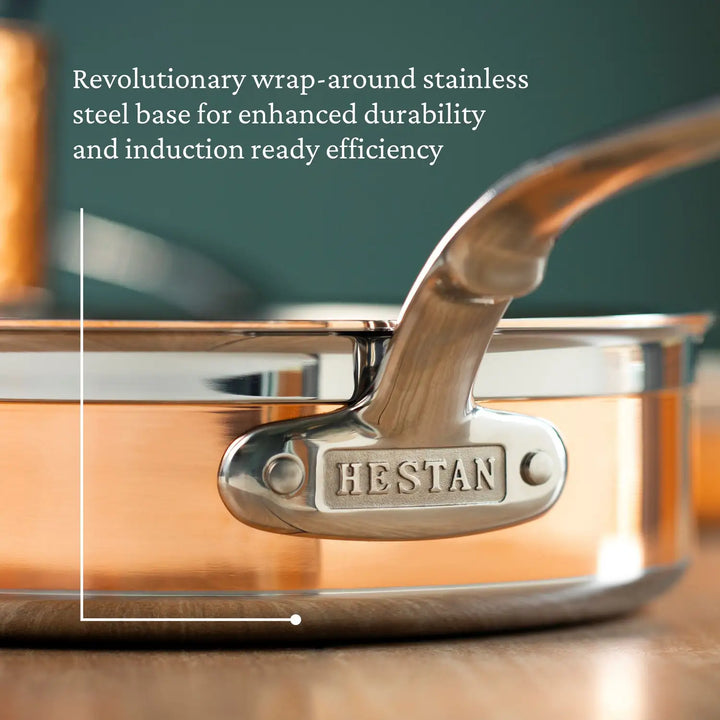 Close-up of the CopperBond Copper Induction Sauté with Lid, 3.5-Quart, showcasing a durable copper core and stainless steel handle engraved with HESTAN. The wrap-around stainless steel base ensures induction compatibility. The softly blurred background adds elegance to the image.