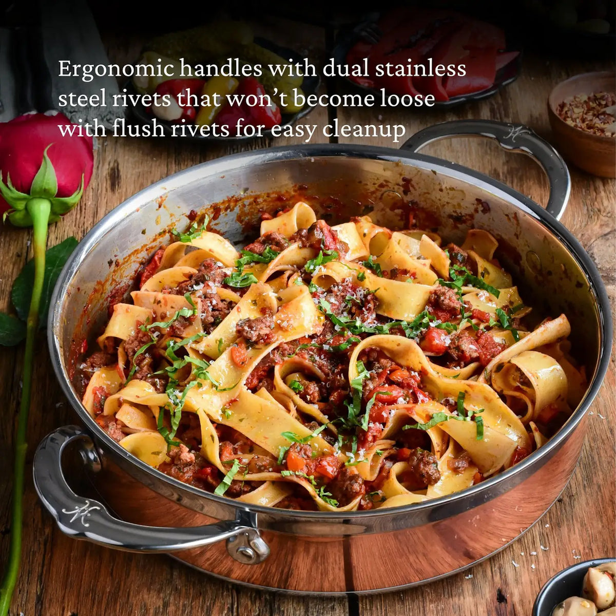 A CopperBond Copper Induction Braiser with Lid (3.5-Quart) filled with pappardelle pasta in meat sauce, garnished with herbs, sits on a wooden table beside spice bowls and a red rose. Text highlights ergonomic handles and oven safe features.