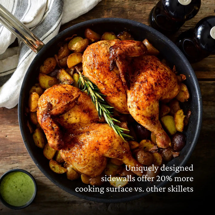 Roasted chicken halves in a skillet with potatoes and rosemary. Text: Unique sidewalls offer 20% more cooking surface vs. other skillets. Made from ProBonds Professional Clad Stainless Steel TITUM® Nonstick Cookware, two dark bottles and a striped cloth rest on the wooden surface nearby.