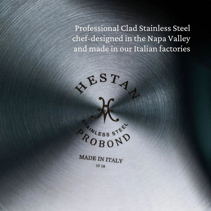 Close-up of a stainless steel cookware surface with engraved text: HESTAN PROBOND Professional Clad Stainless Steel Made in Italy 10 18, featuring TITUM® Nonstick technology. Chef-designed in Napa Valley and made in Italian factories.