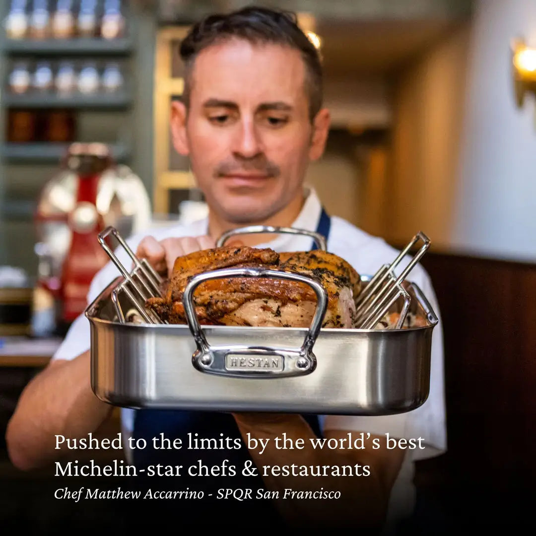 A chef in a white shirt and dark apron holds a Hestan Provisions Nonstick Clad Stainless Steel Roaster with Rack containing roasted meat. Text below reads: “Pushed to the limits by the world’s best Michelin-star chefs & restaurants.”.