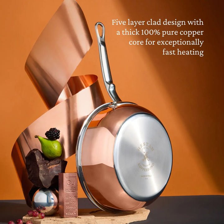 The CopperBond Copper Induction Saucier Pan, 2-Quart with a stainless steel handle is showcased alongside decorative copper elements and fruit, featuring a five-layer clad design with a thick 100% pure copper core for exceptionally fast heating.