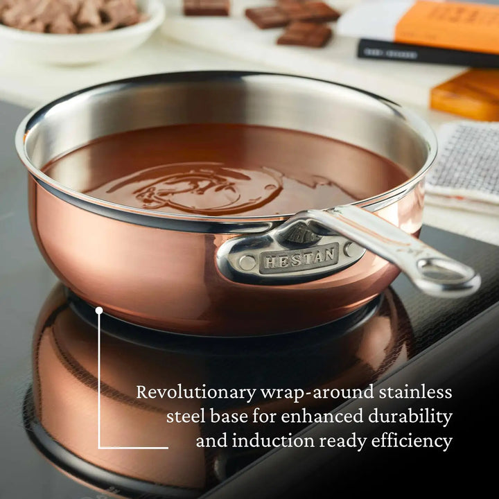 A CopperBond Copper Induction Saucier Pan, 2-Quart, sits on an induction cooktop filled with melted chocolate. The text highlights its wrap-around stainless steel base for enhanced durability and seamless compatibility.