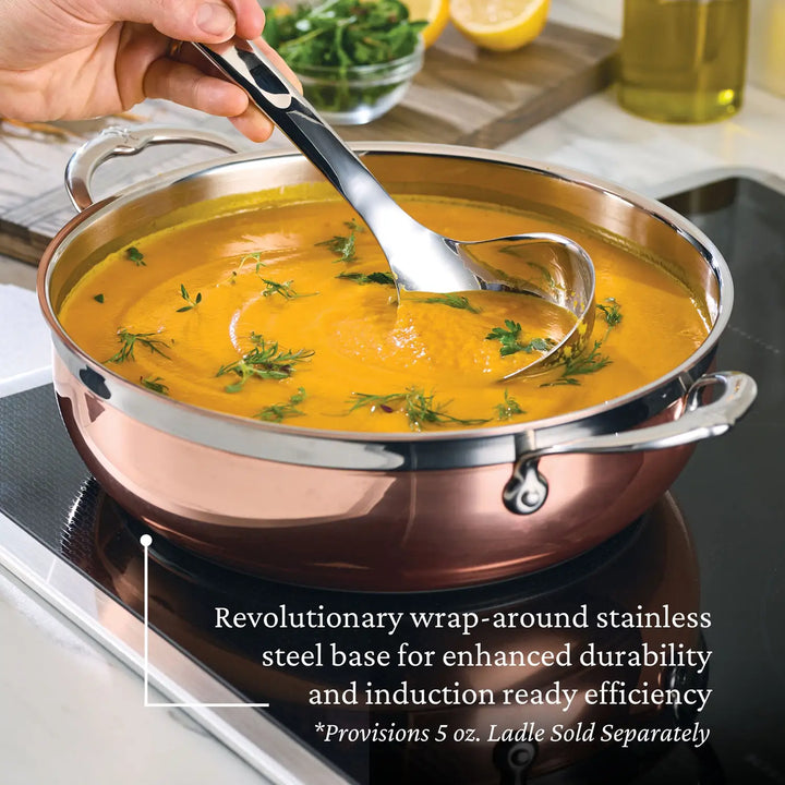 A person stirs orange soup in a CopperBond Copper Induction Dutch Oven, 5-Quart on an induction stove. The pots wrap-around stainless steel base ensures induction compatibility. Fresh herbs and lemon slices are visible in the background, alongside text highlighting the pots features.